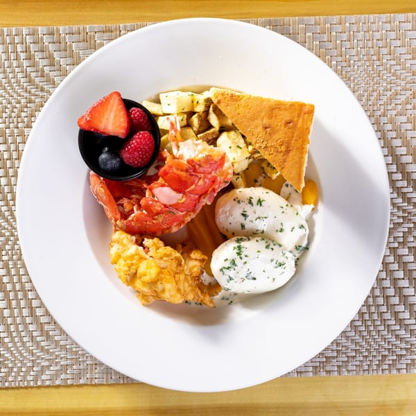 Overhead view of a breakfast plate with lobster, fried potatoes, eggs, cornbread, and berries.
