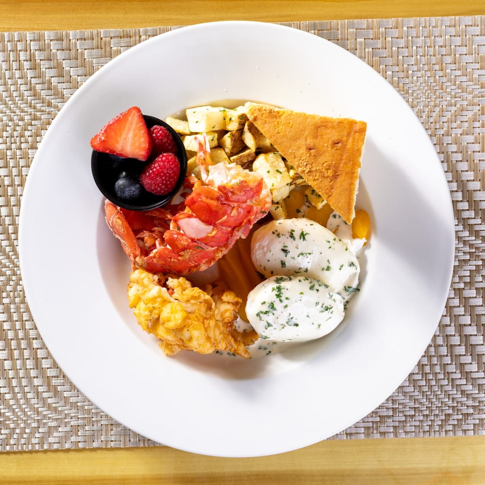 Overhead view of a breakfast plate with lobster, fried potatoes, eggs, cornbread, and berries.
