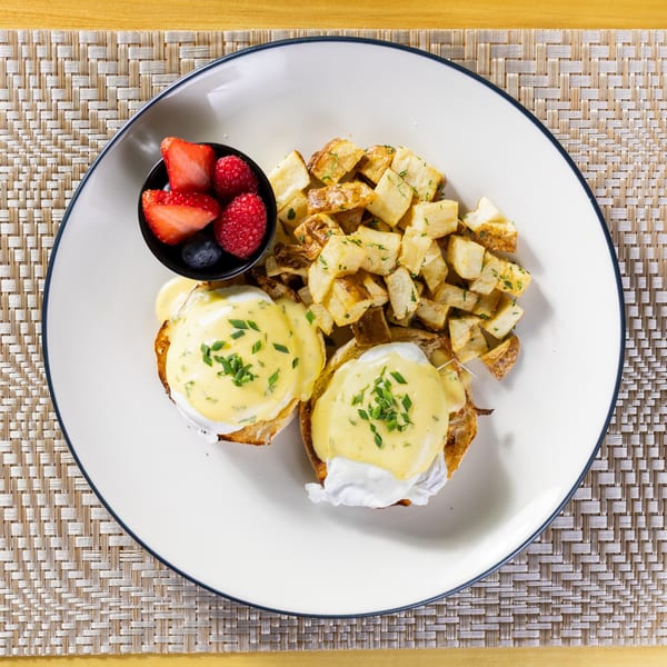 Eggs Benedict with hollandaise sauce and chives, served with home fries and a side of berries.