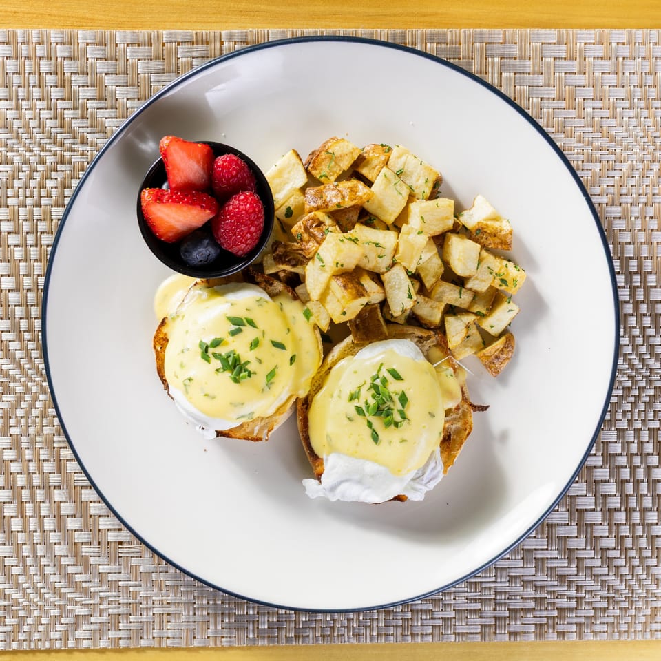 Eggs Benedict with hollandaise sauce and chives, served with home fries and a side of berries.