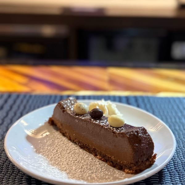 A chocolate dessert bar with white and dark chocolate candies, powdered sugar, and whipped cream.