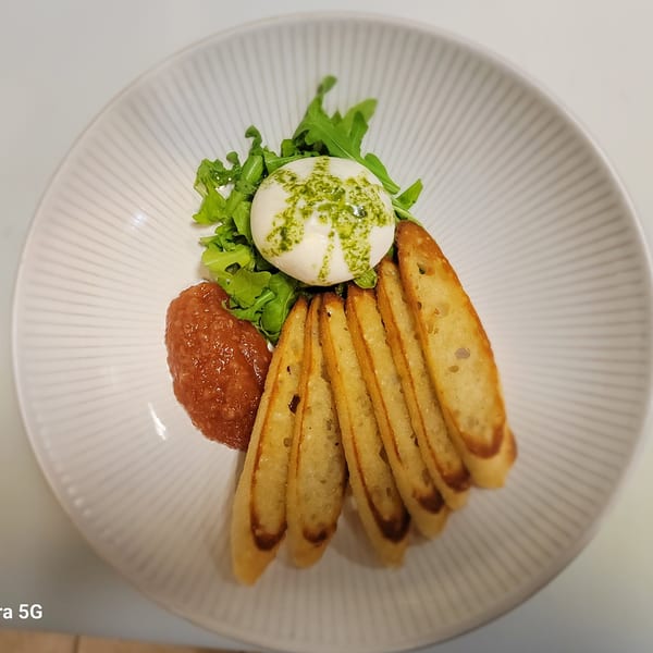 Burrata cheese with pesto, arugula, tomato jam, and toasted bread slices on a white plate.
