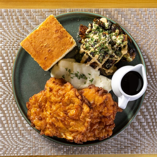 Fried chicken, mashed potatoes, cornbread, roasted Brussels sprouts, and gravy on a green plate.