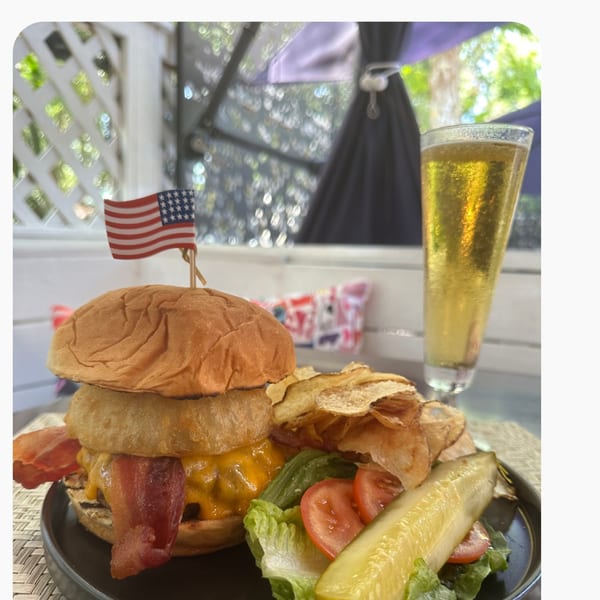 A bacon cheeseburger with onion rings, chips, salad, pickle, and a beer on an outdoor patio.