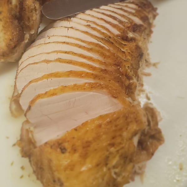 Sliced roasted turkey breast with crispy skin on a white cutting board, with a knife visible.