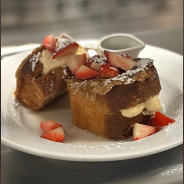 Two pieces of French toast stuffed with cream, topped with strawberries and powdered sugar.
