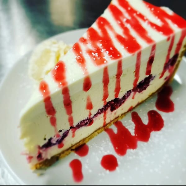 A slice of cheesecake with raspberry filling and red sauce drizzled on top, served with cream.