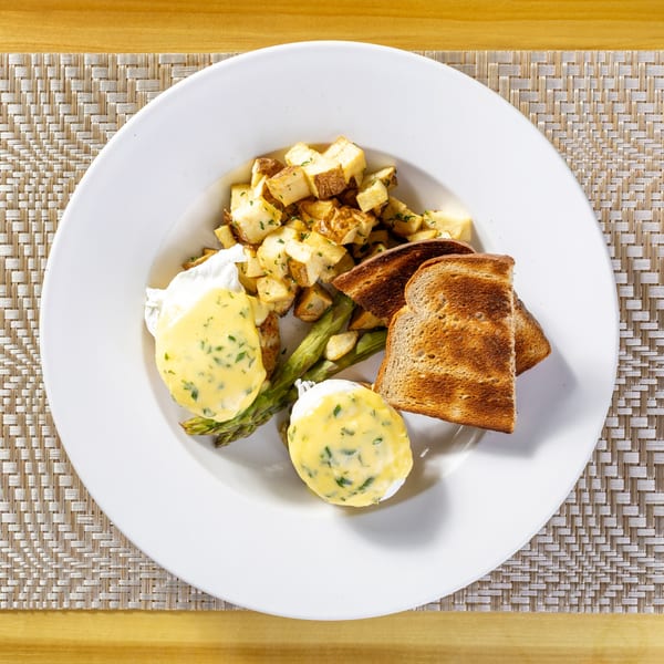 Eggs Benedict with hollandaise sauce, asparagus, home fries, and toast on a white plate.