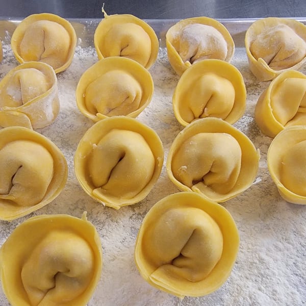 Rows of freshly made, uncooked tortellini pasta dusted with flour on a baking sheet.