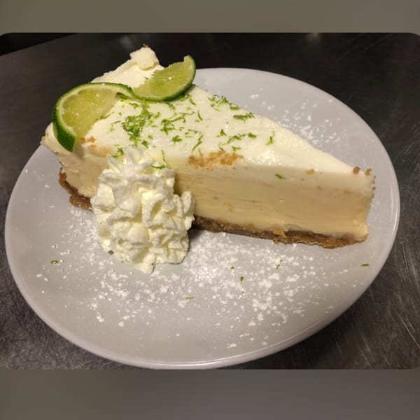 Slice of key lime pie with whipped cream, lime slices, and zest on a white plate.