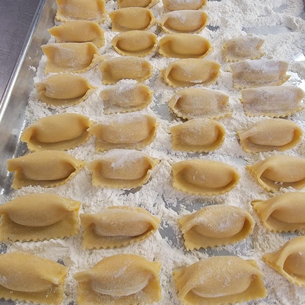Rows of fresh, uncooked ravioli dusted with flour on a metal baking sheet.