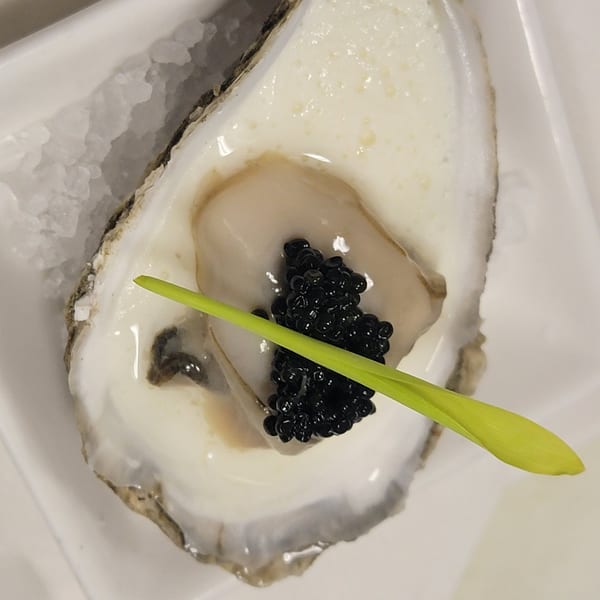 A fresh oyster on a bed of ice, topped with black caviar and a green garnish.