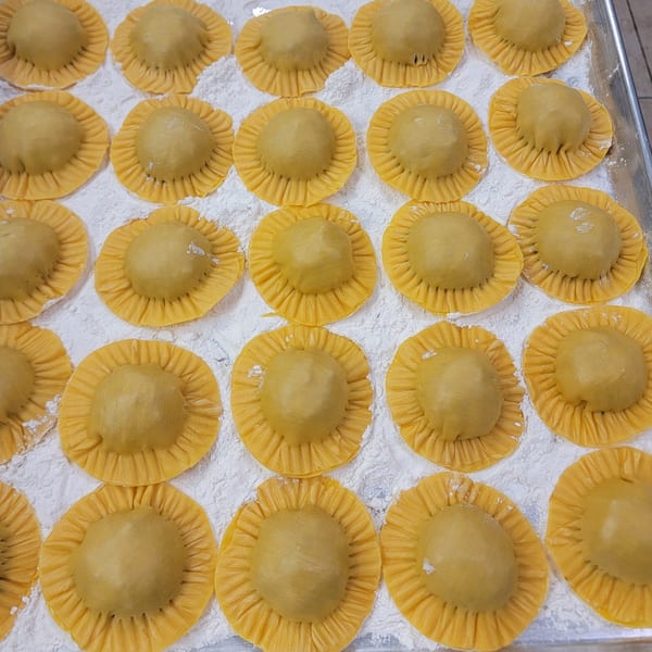 Rows of freshly made, uncooked ravioli with ruffled edges, dusted with flour on a baking sheet.