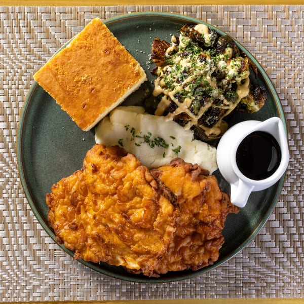 Fried chicken, mashed potatoes, cornbread, roasted Brussels sprouts, and gravy on a green plate.