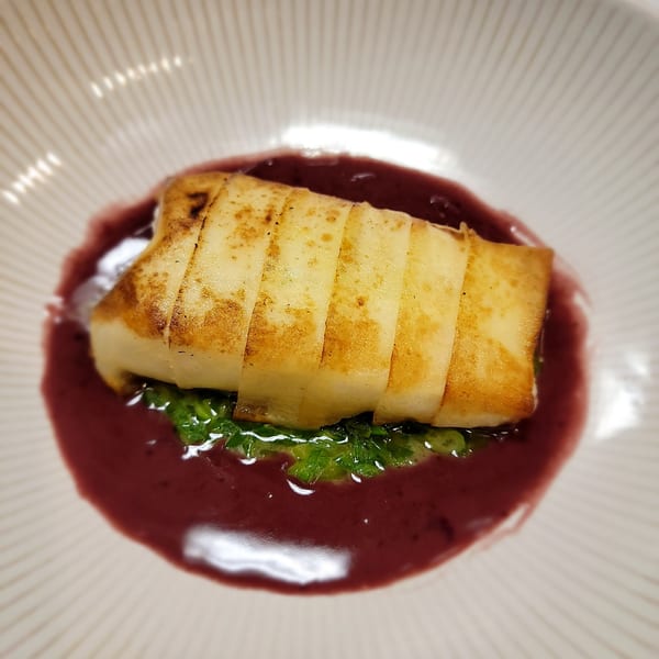 Pan-seared fish fillet with a golden crust, served on green herbs in a rich red sauce.